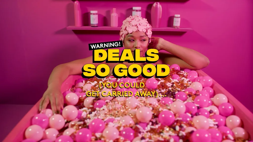 Woman lying in a pink ball pit beneath a Deals So Good caption