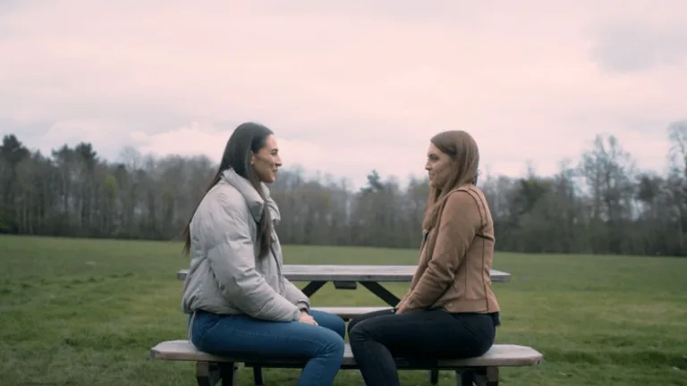 Two women talking at a picnic table in a field