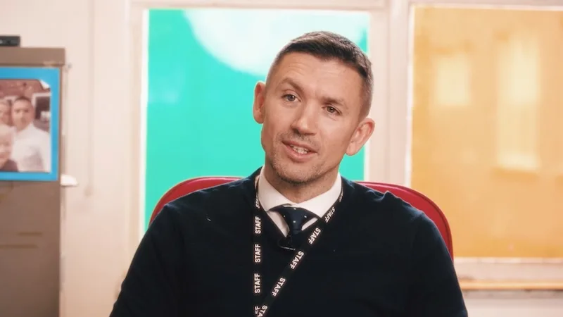 Man in a lanyard and tie speaking during an interview